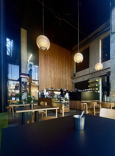 Interior view of Kopi Cafe with timber wall, pendant lights, and tall concrete volume.