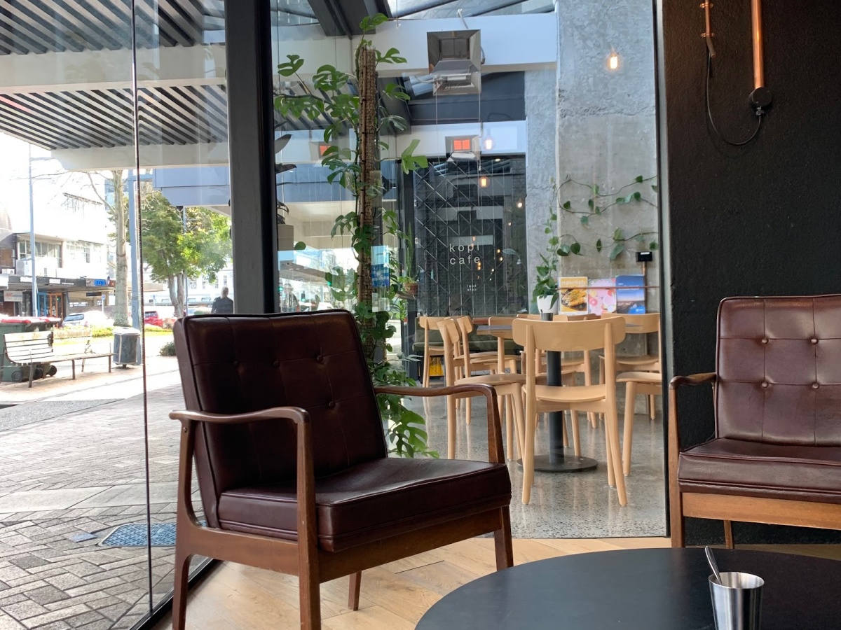 Street-facing window view at Kopi Cafe with lounge seating and the Riverbank Lane frontage beyond.